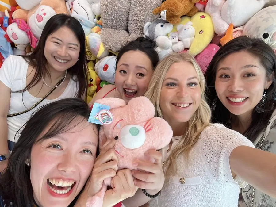 Five of the Magic Garden team laughing together with a pink soft toy, in front of a wall of plush toys.
