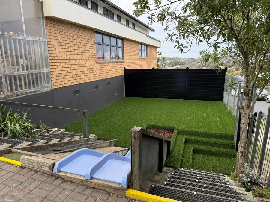 The outdoor stage at Northcross: a turfed platform with steps, a black fence and the brick centre building beside it.