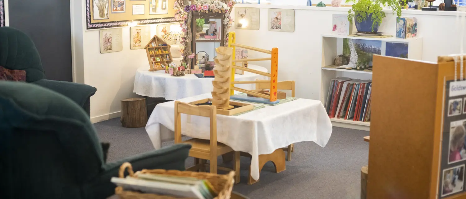A Magic Garden room with a green armchair, a wooden marble run on a small table, book shelves and children's work on the walls.