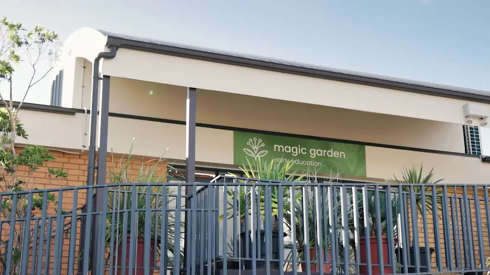 The Magic Garden sign on the deck railing, in front of the brick building.