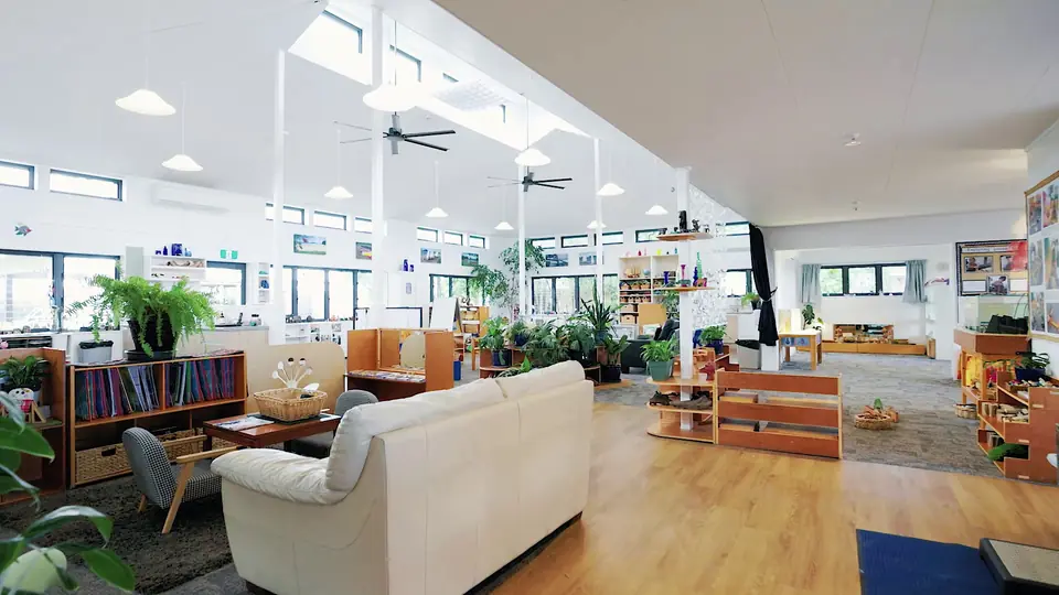 A room with a white sofa, low bookshelves and plants under a high white ceiling.