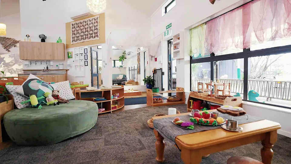 A green ottoman and a table of play food, with silk curtains in the window behind.