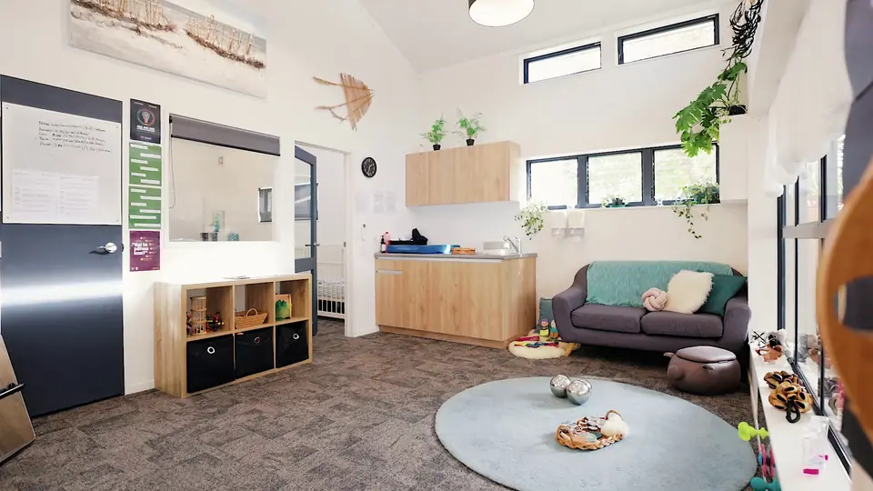 A room with a grey sofa, a round grey rug and a kitchen bench along the wall.