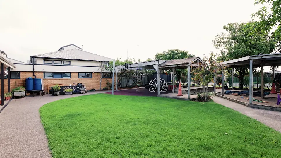 A curved lawn edged by a path, with timber pergolas and the brick centre building behind.
