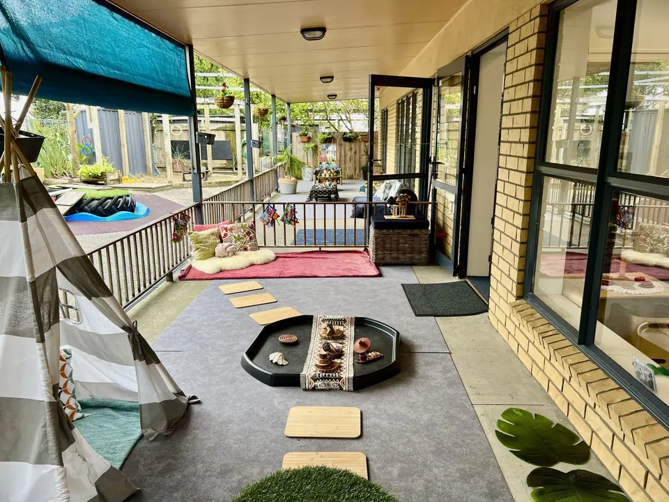 The covered deck, with a striped tepee, stepping pads, cushions on a red rug and a tray of loose parts on a grey mat.