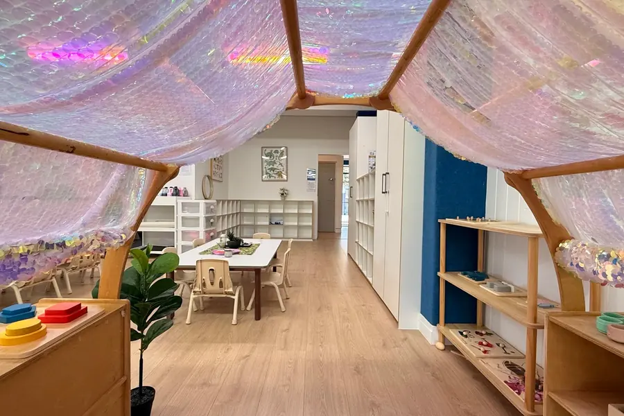 The toddlers’ room at Anzac Street, Takapuna: a sequin canopy hung over the way in, small tables and chairs, white cube shelving and low wooden shelves of materials.