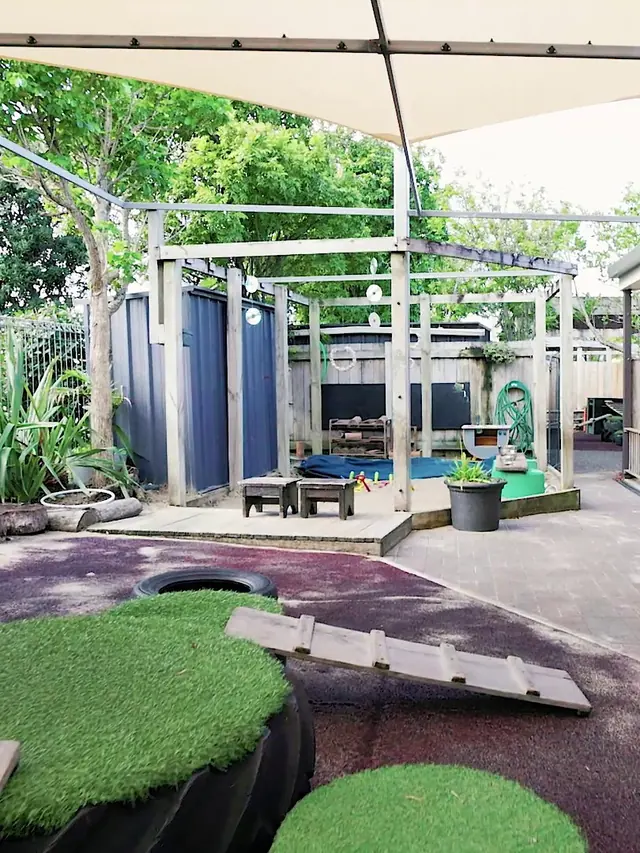 The outdoor play area at Northcross, with turf mounds, a plank bridge and a shade sail over the play area.