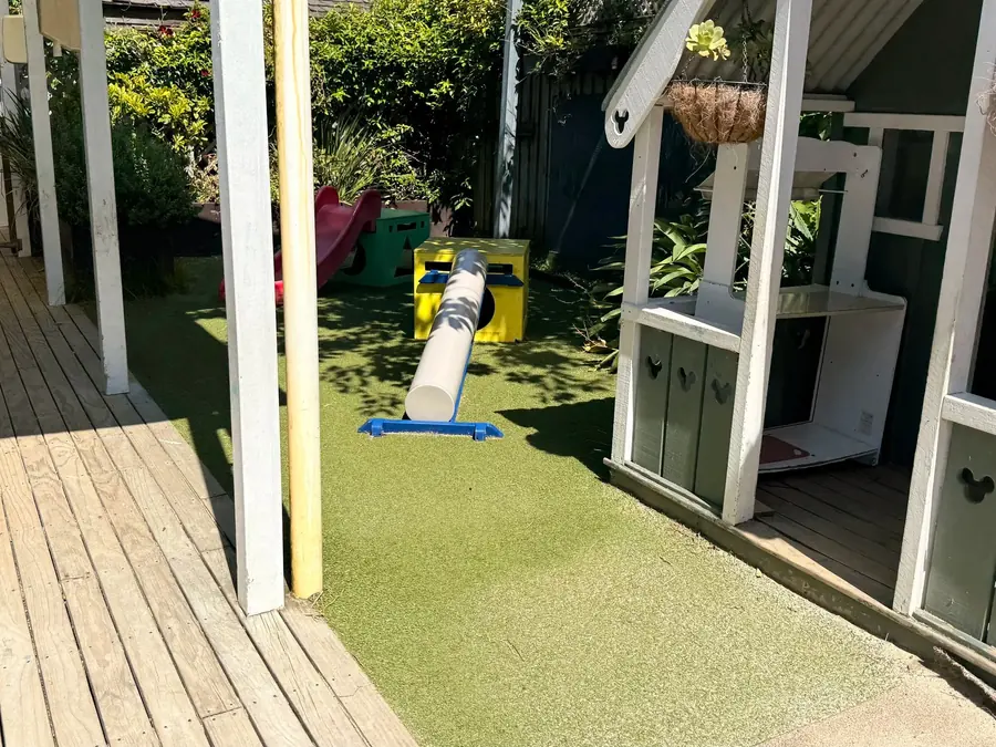 The outdoor deck at Anzac Street, Takapuna, with turf, a tunnel, a slide and a painted playhouse with hanging baskets.